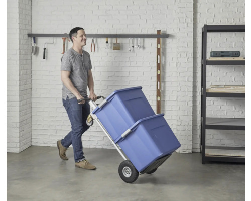 Un homme transporte deux boîtes de rangement bleues avec un diable dans un garage.