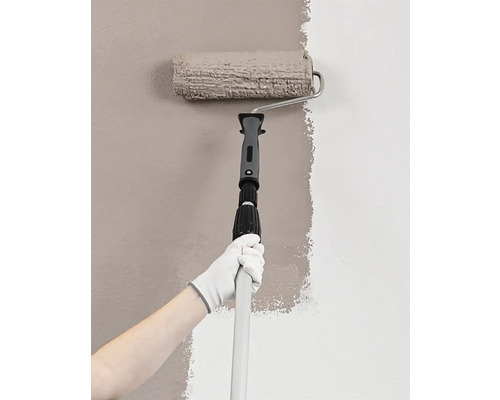 Maler mit Farbroller und Teleskopstiel beim Streichen einer Wand