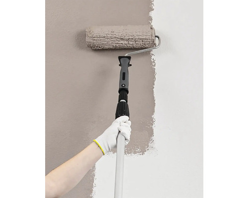 Une personne peint un mur avec un rouleau de peinture sur un manche télescopique.