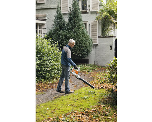 Un homme utilise un souffleur de feuilles dans le jardin pour enlever les feuilles.