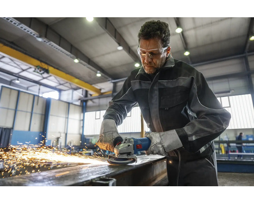 Ein Mann schleift mit einer Schleifmaschine ein Metallstück in einer Werkstatt.