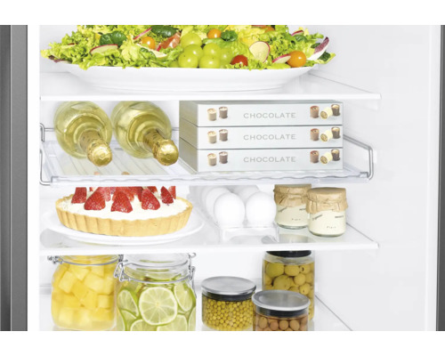 Gefüllter Kühlschrank mit Salat, Schokolade, Eiern, Kuchen, Limetten, Ananas und Oliven