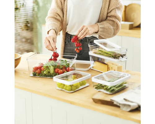 Une femme remplit des boîtes de conservation transparentes avec des légumes et des fruits dans une cuisine.