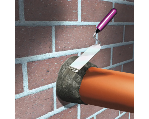 Un maçon remplit un trou dans un mur de briques avec une truelle