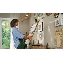 Une femme tient un cadre photo devant un mur avec des cadres déjà accrochés pour créer une nouvelle galerie.