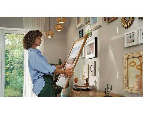 Une femme tient un cadre photo devant un mur avec des cadres déjà accrochés pour créer une nouvelle galerie.