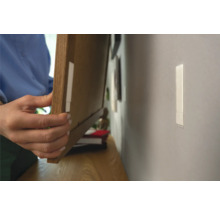 Person befestigt einen Bilderrahmen mit Klebestreifen an der Wand.