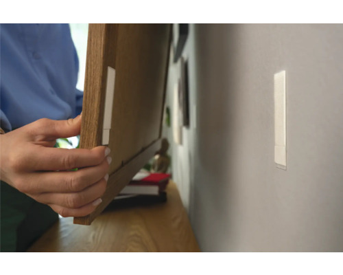 Person befestigt einen Bilderrahmen mit Klebestreifen an der Wand.