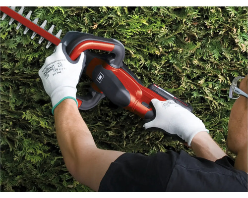 Une personne utilise un taille-haie tout en portant des gants de protection.