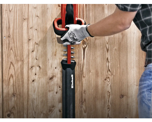 Un homme avec un gant inspecte un taille-haie rouge de Einhell.