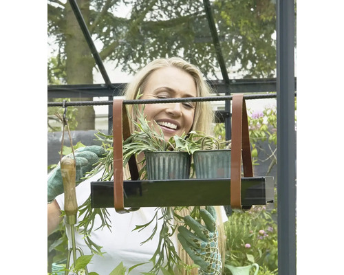 Frau im Gewächshaus mit hängendem Pflanzenregal mit zwei Pflanzen