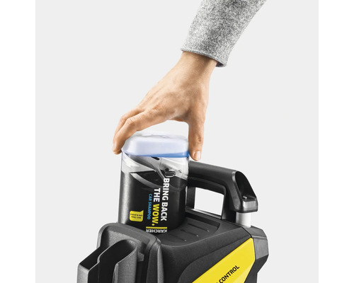 Eine Hand setzt eine Flasche Autoshampoo auf einen Hochdruckreiniger.