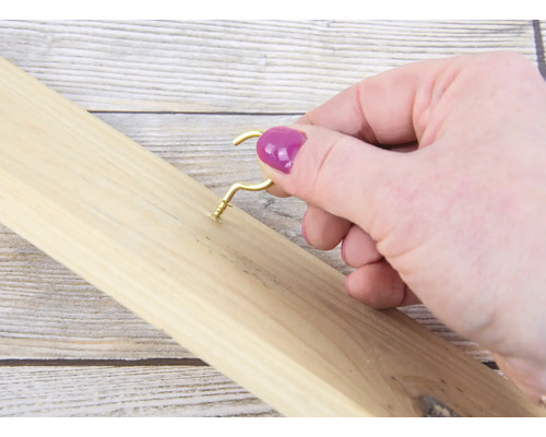 Eine Person schraubt einen goldenen Haken in ein Holzbrett