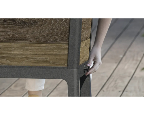 Detailansicht eines Hochbeets mit Holzverkleidung und einer Person, die einen Drehknopf an der Seite bedient