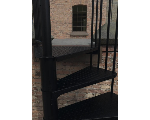 Detailansicht einer schwarzen Wendeltreppe aus Metall vor einer Backsteinmauer.