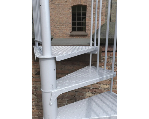 Detailaufnahme einer weissen Wendeltreppe vor einer Backsteinmauer.