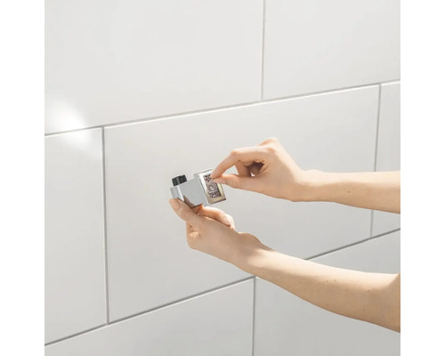 Gros plan d''une main actionnant un bouton-poussoir de thermostat chromé avec des chiffres sur un mur carrelé