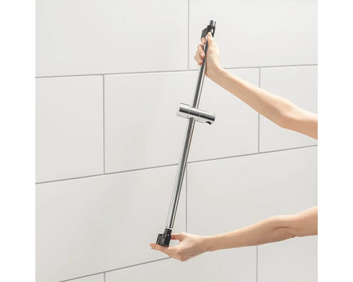 Une personne tient une barre de douche avec support de pommeau de douche devant un mur carrelé.