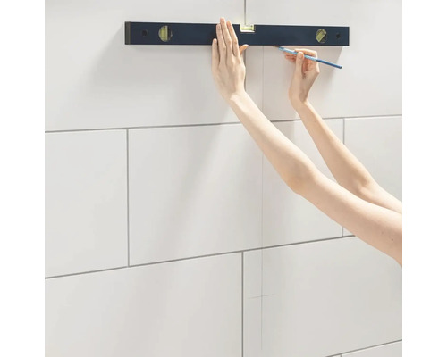 Une personne utilise un niveau à bulle et un crayon pour tracer une ligne sur des carreaux.