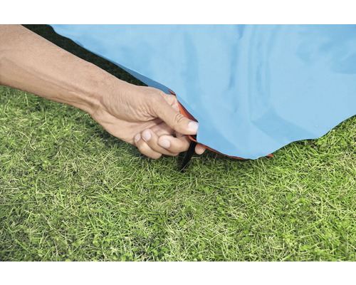 Nahaufnahme einer Hand, die ein Zelt auf einer Grasfläche befestigt.