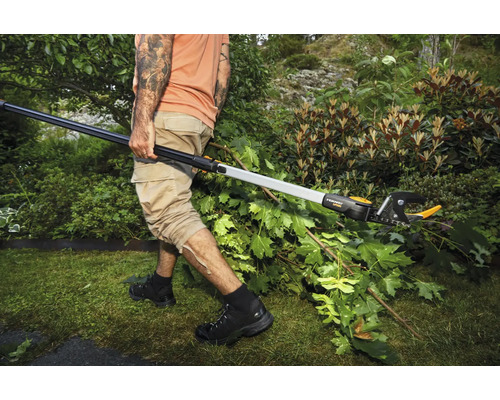 Une personne coupe des branches dans un jardin avec un sécateur télescopique.