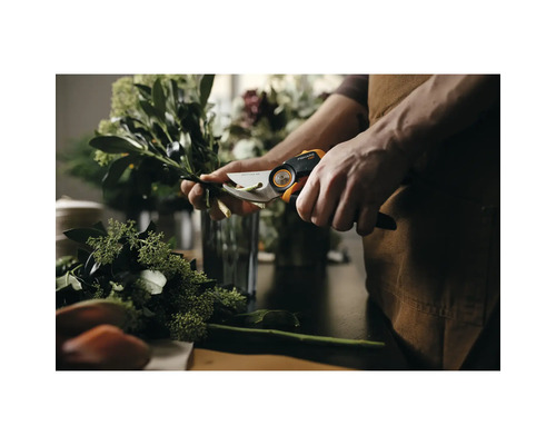 Une personne coupe des branches avec un sécateur Fiskars sur une table.