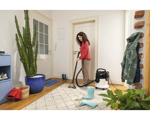Femme nettoie un tapis avec un aspirateur-laveur dans un couloir lumineux.