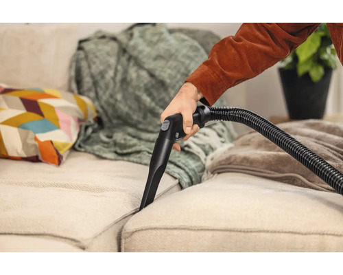 Une personne nettoie un canapé avec un nettoyeur de rembourrage.