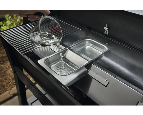 Une personne verse de l''eau d''un verre doseur dans un récipient en acier inoxydable d''un barbecue.