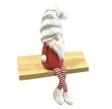 Nain décoratif avec bonnet et jambes rayées assis sur une planche en bois.