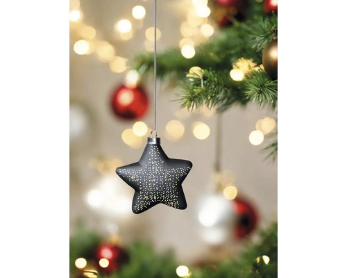 Sternförmiger Christbaumschmuck mit Lichtpunkten hängt an einem Weihnachtsbaum.