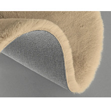 Detailansicht eines beigefarbenen Teppichs mit Felloberfläche und Textilunterseite