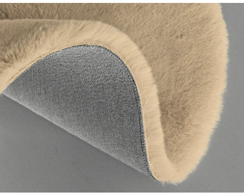 Detailansicht eines beigefarbenen Teppichs mit Felloberfläche und Textilunterseite