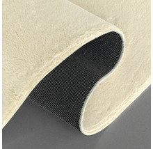 Detailansicht eines beigefarbenen Teppichs mit schwarzer, genoppter Rückseite.