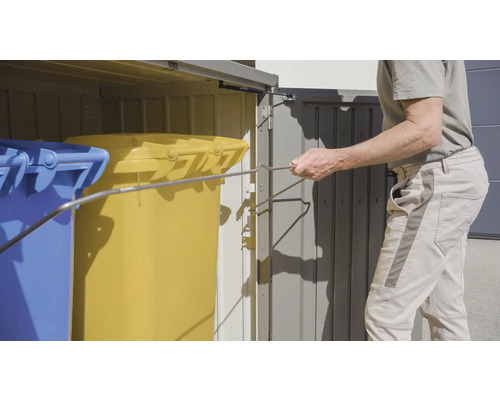 Geöffnete Mülltonnenbox mit zwei Mülltonnen und einem Mann, der eine Mülltonne entleert.