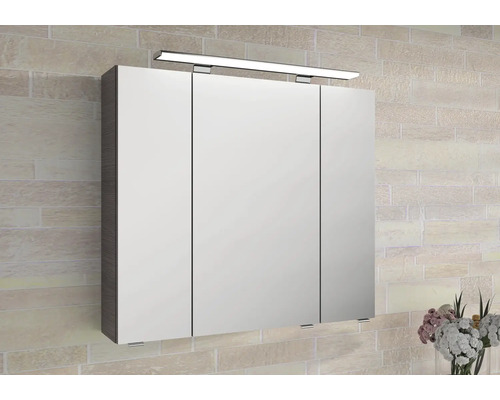 Dreitüriger Spiegelschrank für das Badezimmer mit LED-Beleuchtung und dunklen Seitenpaneelen an einer Wand in Steinoptik.