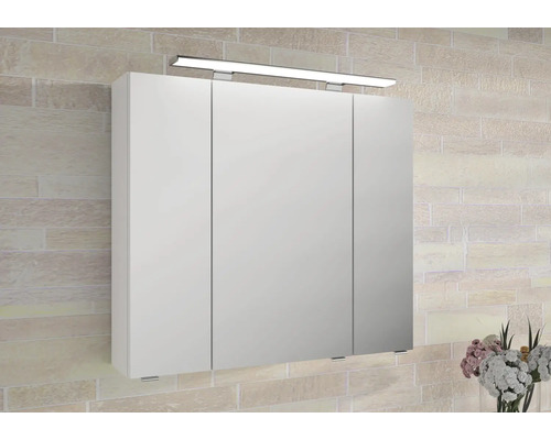 Dreitüriger Spiegelschrank mit LED-Aufsatzleuchte an einer Wand in Ziegeloptik.