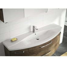 Moderner Waschtisch mit geschwungenem weißem Waschbecken, Einhebelmischer und Unterschrank in Holzoptik vor gefliester Wand.