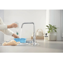 Eine Person füllt Wasser aus einer Flasche in eine blaue Schüssel unter einem Wasserhahn