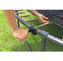 Une personne fixe un ressort au cadre du trampoline avec un tendeur