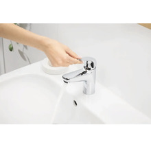 Une main actionne un robinet brillant sur un lavabo.