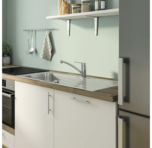 Küchenszene mit Spüle, Armatur, Arbeitsplatte und Küchenutensilien an der Wand