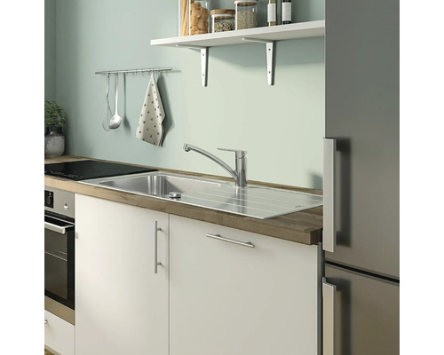 Küchenszene mit Spüle, Armatur, Arbeitsplatte und Küchenutensilien an der Wand