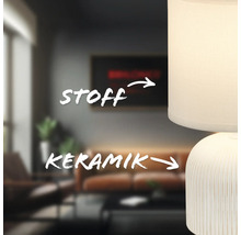 Nahaufnahme einer Tischleuchte mit Lampenschirm aus Stoff und Keramikfuß in einem Wohnzimmer.