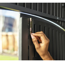 Une personne actionne un loquet sur une porte de jardin pour la sécuriser.