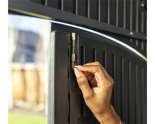 Une personne actionne un loquet sur une porte de jardin pour la sécuriser.