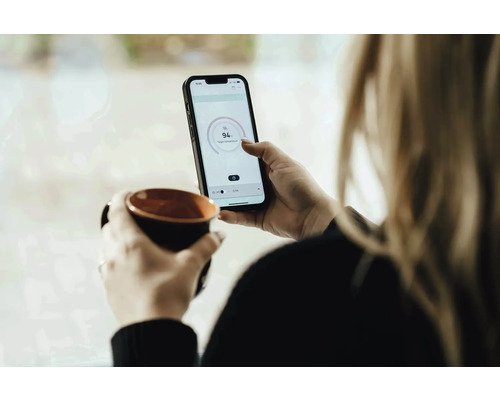Femme avec tasse et smartphone pour le contrôle de la température