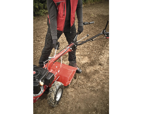 Une personne utilise une motobineuse rouge dans un champ