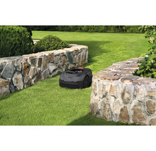 Ein Rasenmähroboter auf einer Rasenfläche zwischen zwei Steinmauern.