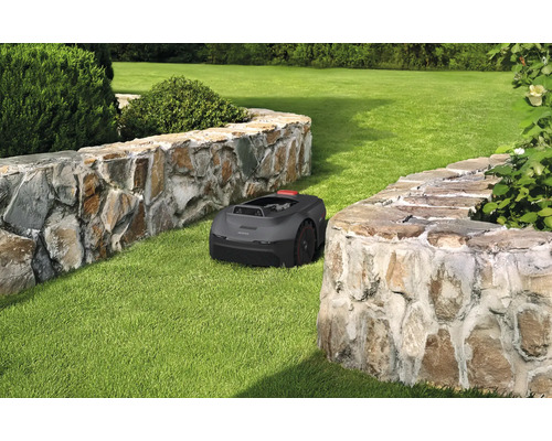 Ein Rasenmähroboter auf einer Rasenfläche zwischen zwei Steinmauern.